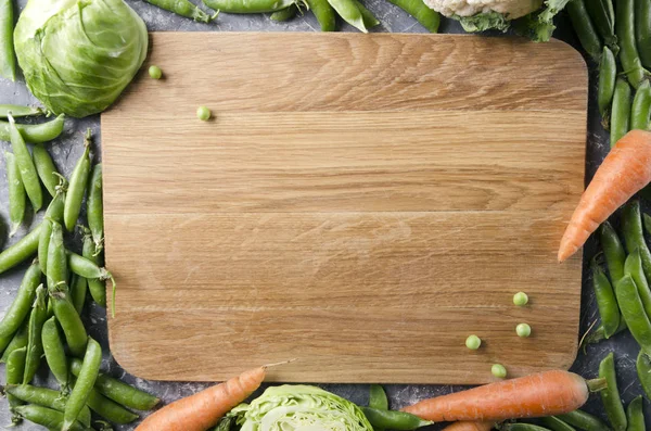 Concept of healthy food and recipes.Cutting board and lot of green spring vegetables such as green peas,carrots, young cabbage.Empty space for design