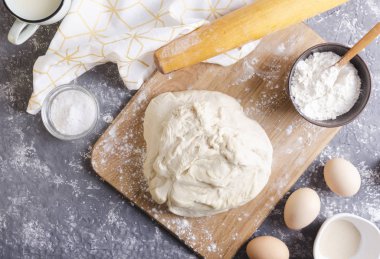 Taze yapılmış hamur ahşap tahta, yumurta, un kase, tuz, fincan süt, makaralı pin ve peçete gri masa, üst görünüm. Hazırlama sürecinin kavramı yoğurma