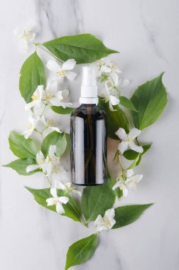Beyaz yüzeyde cam şişe ve Yasemin çiçekleri üst görünümü. Yasemin yağı ile güzellik tedavileri kavramı