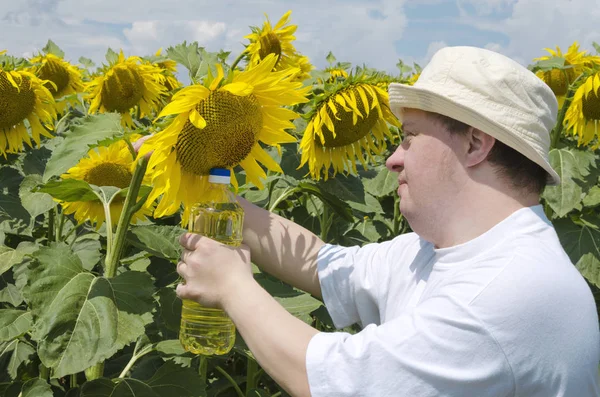 Young man with down syndrome as a farmer holding bottle of sunflower oil. Beatiful sunflower field