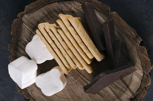 Top view of ingredients for s`mores.Cookies, chocolate and marshmallow on the wooden tray