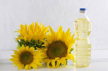 Beyaz duvara karşı beyaz masada ayçiçek yağı plastik şişe ve güzel çiçek açan ayçiçeği