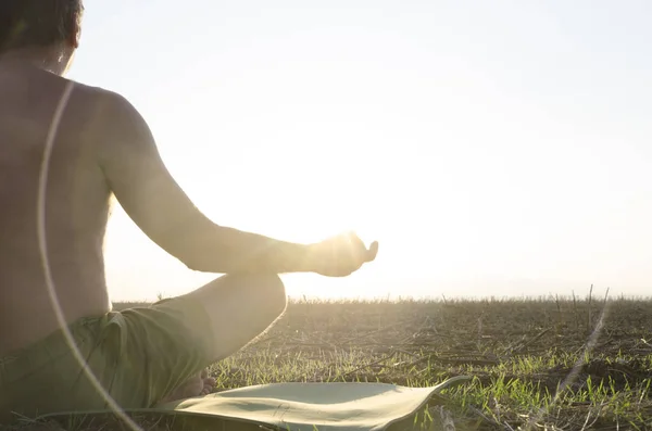 Back of meditating man, who sitting on the mat in the field.Sunset time in the field