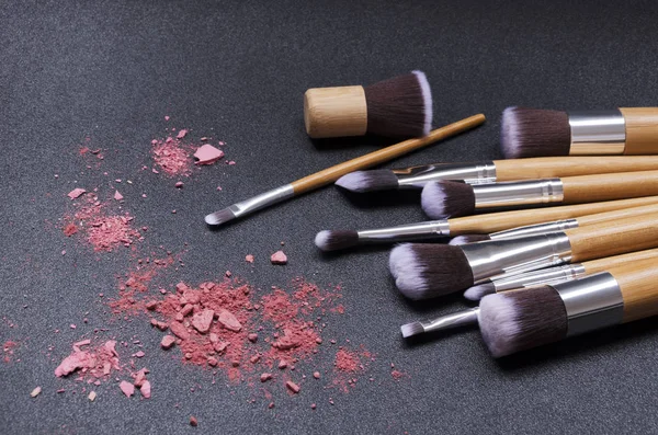 Makeup brushes and crashed blushes on the dark surface. Professional tools for makeup