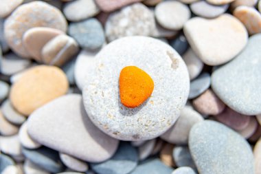 An eye-catching orange triangular pebble centered on a pale grey stone stands out against a bed of varied pebbles, a play button made of stone clipart