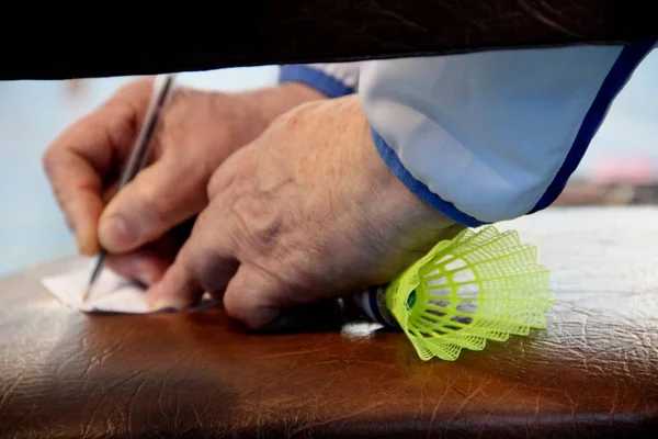 an older trainer takes notes with a shuttlecock for badminton in his fist, framing close-up