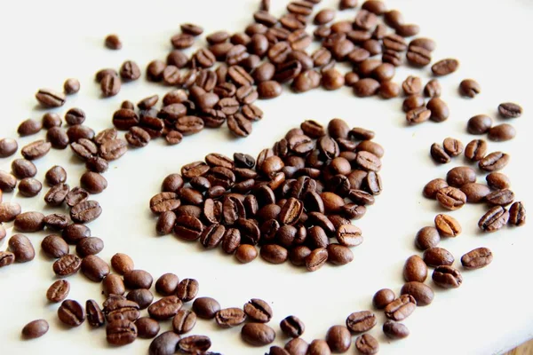 Many scattered on the table roasted coffee beans in the shape of a heart, selective focus — Stock Photo, Image