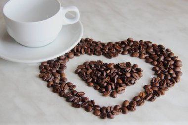 bir kalp şeklinde kahve çekirdekleri, beyaz bir fincan yanında masada kavurma sonra