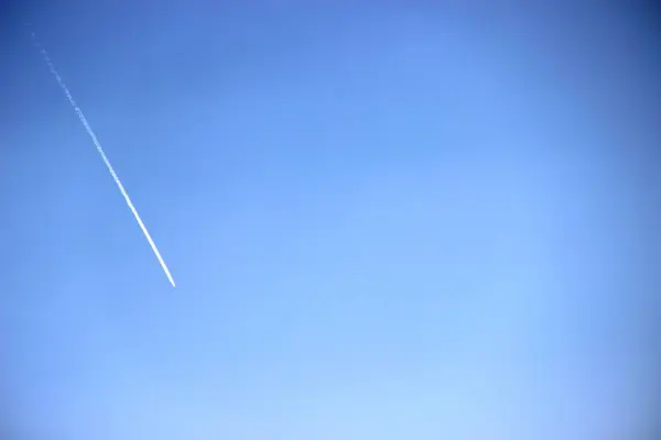 White trace of a plane flying high in the blue sky — 스톡 사진