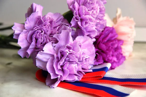 carnation flowers. bouquet of flowers, carnations. violet, lilac and pink flowers carnations in the bouquet. ribbon white-red-blue stripes. Russian symbol