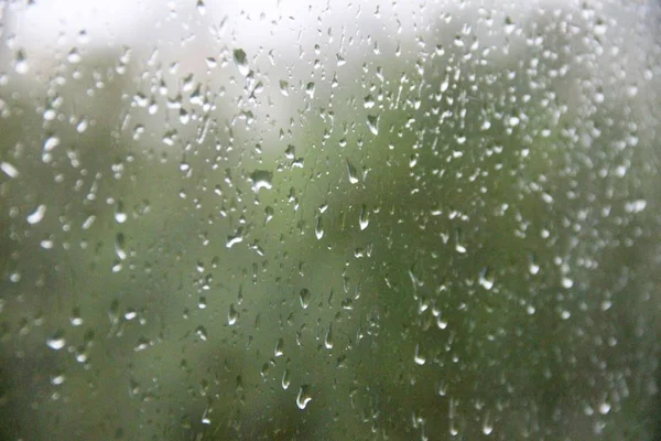 Ventana con grandes gotas de lluvia sobre un fondo verde, gris y urbano. La primera tormenta de verano. Lluvia cae en una ventana —  Fotos de Stock