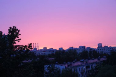 çarpıcı gün batımı, kentsel alanlar, ağaç gölgeler, fabrika bacaları ve yüksek katlı konut binaların siluetleri