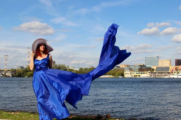 Mujer en un hermoso vestido azul largo como una cola de pez. retrato en pleno crecimiento a orillas del río, en un caluroso día de verano ventoso — Foto de Stock