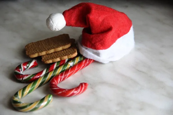 Kırmızı Noel Baba şapkası, üç baston şeker ve bir çift kurabiye. Noel ve yeni yıl tatlıları, Noel cüce şapkası.