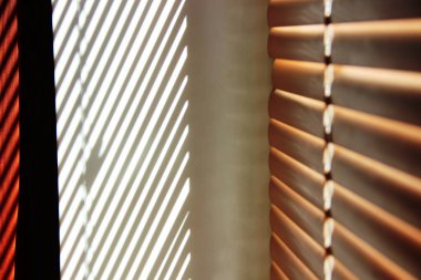 Pencerenin yamacında parlak güneş ışığı, kahverengi perdelerin arasında parlak çizgiler.