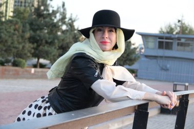 Siyah ceketli bir kadın, bej bir başörtüsü üzerinde siyah bir şapka, eldivensiz şehirde tek başına yürümek. yakın plan portre