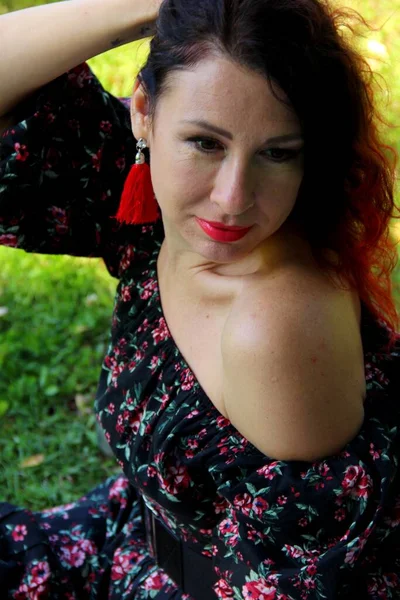 Portrait d'une brune aux cheveux roux et aux boucles d'oreilles écarlates en robe foncée sur la pelouse verte — Photo