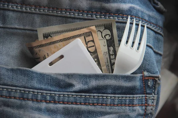 Small American bills, a card key, and a plastic fork in the pocket of the blue jeans of an employee rushing to a lunch break. Fast food concept in a big city. — Stock Photo, Image