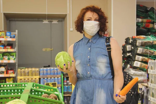 Markette yüzünde tıbbi maske olan kot elbiseli bir esmer. Bir elinde lahana, diğer elinde havuç..