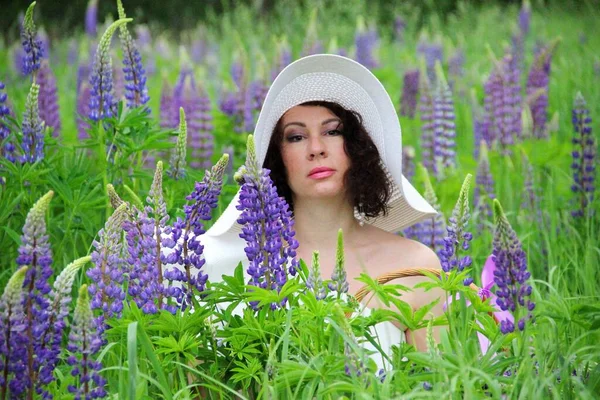 Portrait d'une brune coiffée d'un chapeau blanc dans un champ de lupins fleuris — Photo