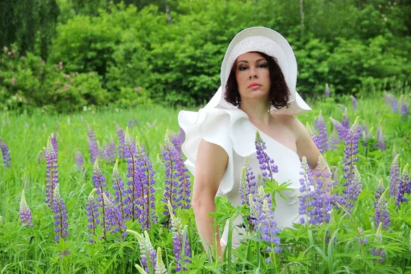 Portrait of a brunette in a white hat in a field of flowering lupins. wood nymph — Stock Photo, Image