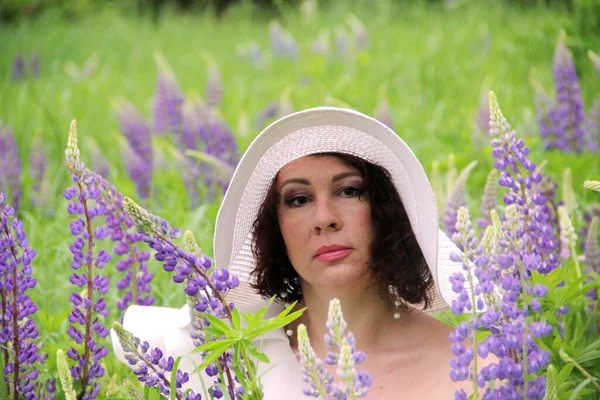 Morena encantadora en un sombrero blanco en un campo de altramuces florecientes, retrato en colores cálidos — Foto de Stock