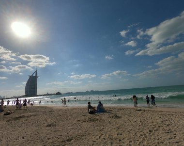 Panoramik görünüm Jumeirah Plajı ve Burj Al Arab ile mavi gökyüzü ve masmavi bir deniz. Kişi ve aileler sahilde zevk. Bulutlar hediye.