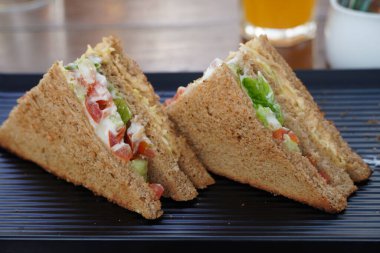 Lokantada siyah bir tabağa yerleştirilmiş iki kulüp sandviçi. Kulüp sandviçin yakın plan fotoğrafı. Prosciutto, sebze, marul ve mayonezli sandviç. Tahta tabakta taze dilimlenmiş çavdar ekmeği. 93JR