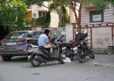 Motosikletinin üstünde oturan ve binanın dışındaki telefona bakan bir adam. : Udaipur Hindistan - Ağustos 2020 2KF