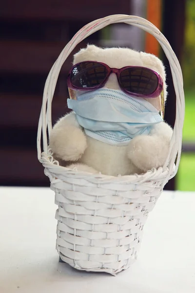 Güneş gözlüklü, beyaz sepetli ve tıbbi maskeli bir oyuncak ayı.