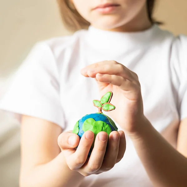 A small globe with trees in the hands of a child. Layout of the globe made of plasticine in childrens palms. Concept
