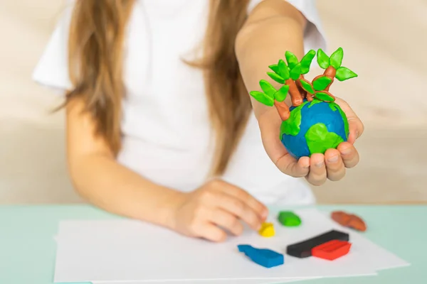Um pequeno globo com árvores nas mãos de uma criança. Layout do planeta feito de plasticina em palmeiras infantis. Conceito — Fotografia de Stock