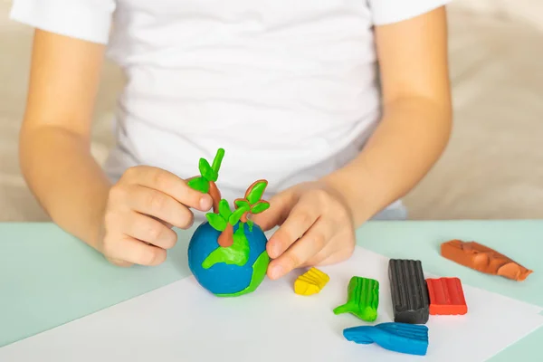 A criança esculpe da plasticina o globo e árvores. Layout do planeta em palmeiras infantis. Ecologia dos conceitos . — Fotografia de Stock