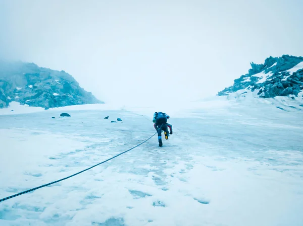 Man climber climbs the mountains with a rope on the glacier. The concept of extreme recreation and adventure.