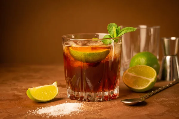 Cocktail aus Rum, Cola-Eiswürfeln und Limette in einem Glasbecher auf dunkelbraunem Hintergrund. stark alkoholisches Getränk. — Stockfoto