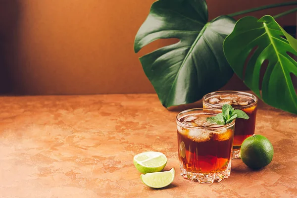 在热带绿叶的背景下, 在玻璃杯中喝朗姆酒或可乐冰块多汁的石灰。复制空间. — 图库照片