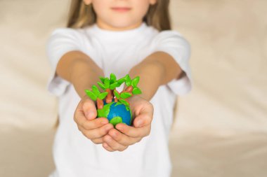 Küçük bir kız elleriyle plastikin yapılmış ağaçlar ile bir model dünya tutar. Küçük bir dünya çocuk avuç içinde yatıyor.