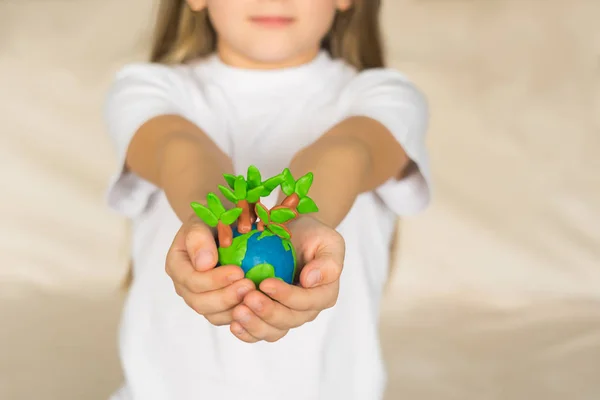 stock image A little girl holds in her hands a model globe with trees made of plasticine. A small globe lies in the palms of child.