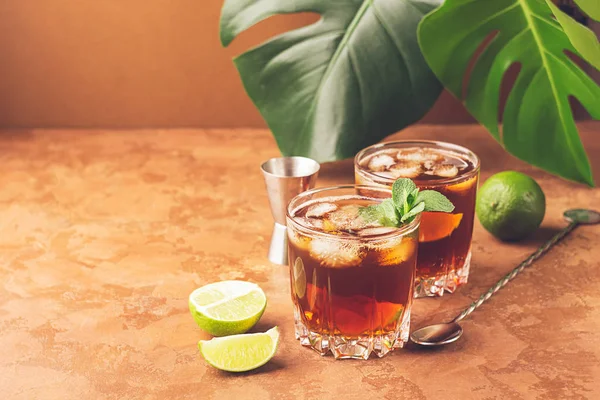 Cocktail da rum e cubetti di ghiaccio di cola in occhiali di vetro foglie verdi di una pianta tropicale lo sfondo marrone scuro. S — Foto Stock
