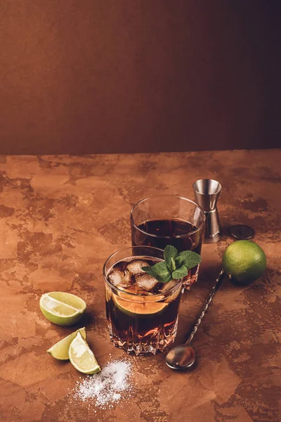 Cóctel de ron y cubos de hielo de cola y lima en un vaso de vidrio sobre un fondo marrón oscuro. Bebida alcohólica fuerte . — Foto de Stock