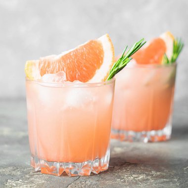 Açık gri beton arka planda biberiye greyfurt ve buz camı kadeh iç. Serinletici yaz kokteyli yakın çekim.