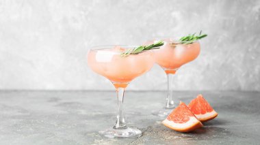 Gri beton arka planda greyfurt biberiye ve buz iki zarif cam kadehler iç. Serinletici bir yaz kokteyli.