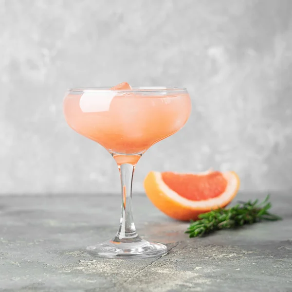 Pij rozmaryn grejpfruta i lód w eleganckim szklanym kieliszkiem na szarym, betonowym tle. Orzeźwiający letni koktajl. — Zdjęcie stockowe