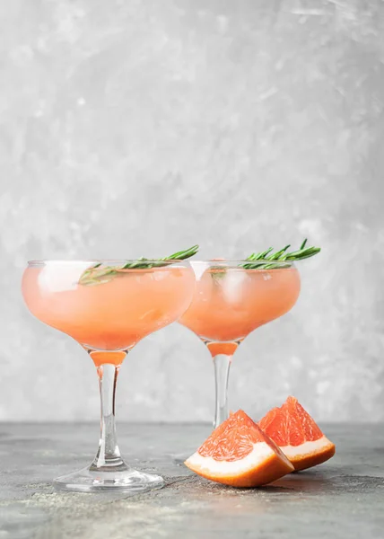 Bere pompelmo rosmarino e ghiaccio due eleganti calici di vetro su sfondo grigio cemento. Un rinfrescante cocktail estivo . — Foto Stock