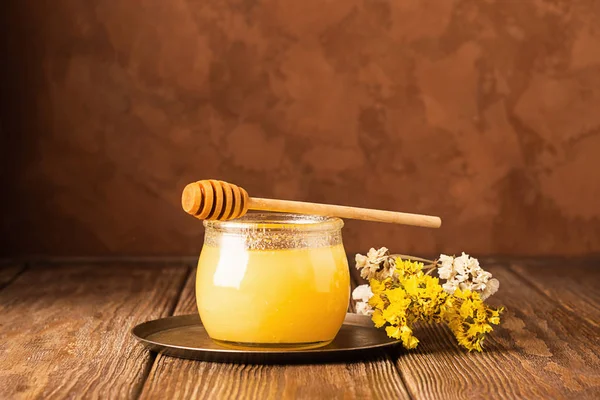 Банка с золотистым свежим пчелиным медом и медовая ложка на коричневом деревянном фоне. Концепция натуральных продуктов . — стоковое фото