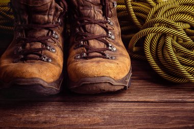 Bir çift kahverengi yıpranmış botları ve ahşap arka plan üzerinde bir spor ip. Seçici odak. Kavramı seyahat ve macera.