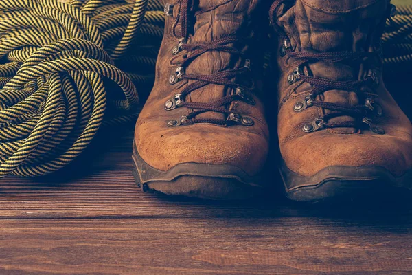 Bir çift kahverengi yıpranmış botları ve ahşap arka plan üzerinde bir spor ip. Seçici odak. Kavramı seyahat ve macera.
