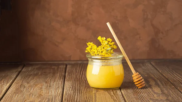Un frasco de miel dorada fresca y una cuchara de miel sobre un fondo de madera sobre la mesa. El concepto de productos naturales . — Foto de Stock