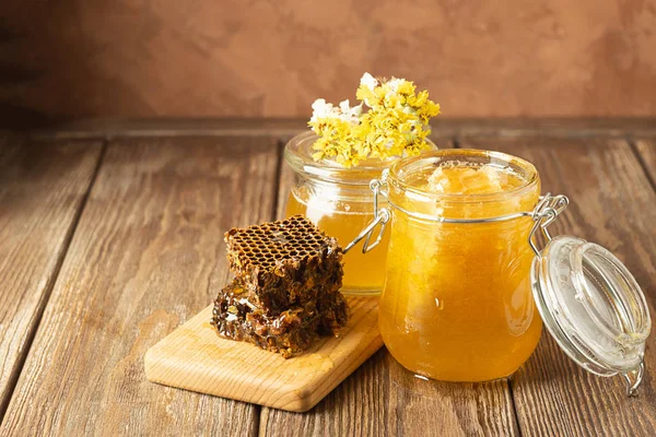 Miel fresca dorada en varios frascos de vidrio y panales sobre mesa de madera. Concepto de alimentos orgánicos. Fondo marrón rústico — Foto de Stock