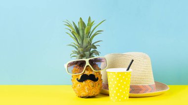 Siyah bıyıklı gözlükkomik giyimli ananas, bir içki ile hasır şapka parlak sarı mavi arka plan ile bir bardak.